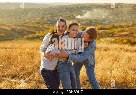 Überglückte Familie, die sich mit Liebe umarmen und Spaß haben, freudig lachen, in der Natur posieren Stockfoto