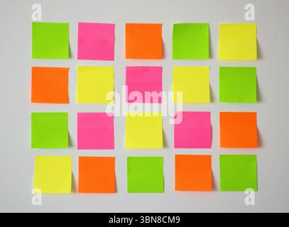 Organisiertes Raster aus zwanzig bunten Haftnotizen aus nächster Nähe, Rosa, Gelb, Orange und Grün, ordentlich auf einer hellweißen Wand angeordnet. Minimal und sauber. Stockfoto