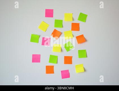 Zufällig platzierte Haftnotizen in Rosa, Gelb, Grün und Orange, die auf einer weißen Wand verstreut sind, symbolisieren Planung, Brainstorming und Erinnerungen. Stockfoto