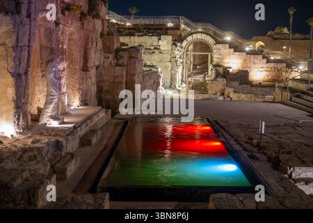 Archäologische Stätte im alten cäsarea israel bei Nacht. Moderner Pool mit Wasser an der Stelle des alten antiken Badezimmers mit alter Statue in der Nähe des Pools und Blick auf alte Bögen und Treppen. Farbbeleuchtung Stockfoto