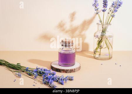 Glasflasche mit ätherischem Lavendelöl und frischen Lavendelblüten auf beigefarbenem Tisch mit Schatten. Aromatherapiekonzept. Stockfoto