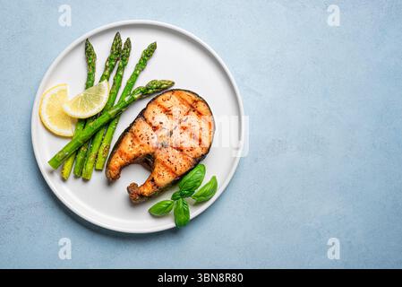 Gegrilltes Lachssteak mit grünem Spargel und Zitronenscheiben auf blauem Hintergrund, Draufsicht, Kopierraum. Ausgewogene gesunde Mahlzeit, Keto-Mittagessen mit Fett, Prote Stockfoto