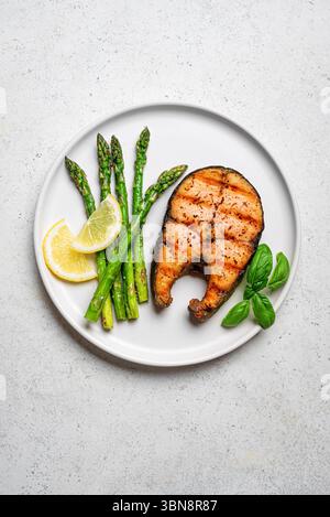 Gegrilltes Lachssteak mit grünem Spargel und Zitronenscheiben auf weißem Betonhintergrund, Blick von oben. Ausgewogene gesunde Mahlzeit, Keto-Mittagessen mit Fett, Protein Stockfoto