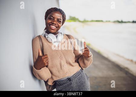 Porträt einer jungen glücklichen schwarzen Frau mit Zahnspangen. Sie sieht in die Kamera und zeigt die Daumen hoch. Stockfoto