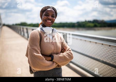 Glückliche junge schwarze Frau schaut in die Kamera und lächelt. Sie genießt einen sonnigen Tag im Freien. Stockfoto