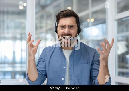 Ein verärgerter Kundendienstmitarbeiter drückt Frustration aus, während er ein Headset trägt und mit seinen Händen Gesten drückt. Stockfoto