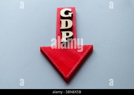 Ein roter Pfeil zeigt nach unten, mit Holzblockbuchstaben mit der Schreibweise „GDP“. Rückgang des Bruttoinlandsprodukts, Konjunkturrückgang, Rezession Stockfoto