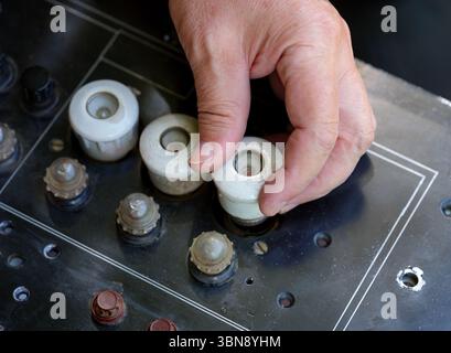 Nahaufnahme eines Arbeiters, der eine weiße keramische Steckersicherung in eine alte schwarze Schalttafel einschraubt Stockfoto