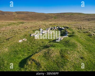 Ein ruhiger Blick auf ein traditionelles Boot in Collaster, Unst, Shetland, vor einer riesigen grasbewachsenen Landschaft unter einem klaren blauen Himmel. Stockfoto