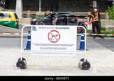 Ein Schild auf Englisch „Acht auf BETRÜGER!“ Wird auf einer Rollbarriere in einem öffentlichen Bereich angezeigt. Bangkok, Thailand, 'wenn ein Fremder bittet, es zu sehen... Geld' Stockfoto