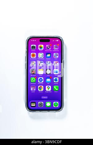 Das iPhone 14 Pro Smartphone zeigt farbenfrohe Apps auf dem Startbildschirm auf einem violetten Hintergrund, isoliert auf einer weißen Oberfläche Stockfoto