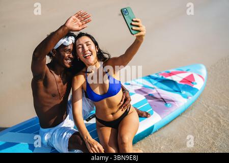 Vielfältige Paare verbunden, mit Technologie und sozialen Medien, während Sie Momente am Strand genießen Stockfoto