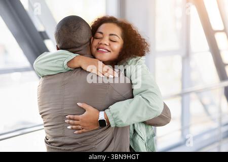 Junge Schwarze Frau umarmt Mann fest am Flughafen, warmer Moment des Wiedersehens Stockfoto