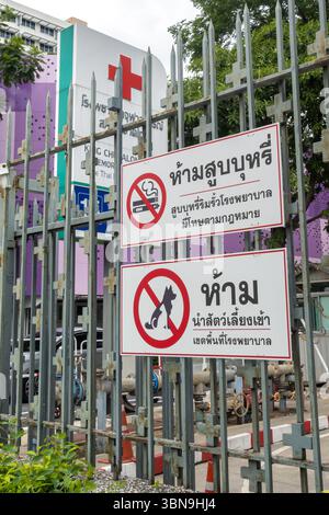 Ein thailändisches Schild auf einem Metallzaun vor einem medizinischen Gebäude mit rotem Kreuz warnt vor Rauchen, Verdampfen und Wandertieren. bangkok, Thailand Stockfoto