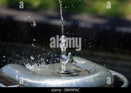 Wasserfontänen strömen in die Luft. Konzentrieren Sie sich auf Metallhähne mit Wasser, das um ihn herum kaskadiert und Tropfen beim Aufprall mit Edelstahlbecken explodieren. Stockfoto