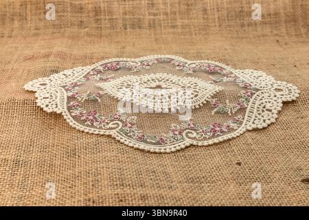 Deckchen aus Vintage-Spitze mit Blumenstickerei auf rustikalem Sackleinen-Stoff. Gemütliches dekoratives Element für Küche, Esszimmer, Tischeinrichtung, Shabby Chic und Cottage Stockfoto