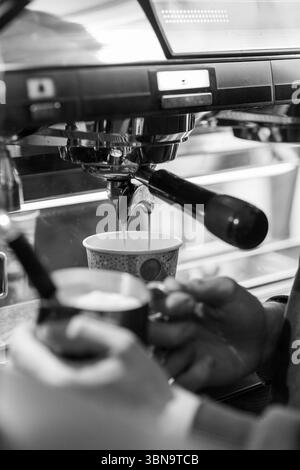 Espresso wird in einem Café mit einem Barista zubereitet, indem er im Morgenlicht eine Maschine zum Extrahieren von Kaffee verwendet Stockfoto