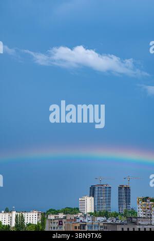 Der farbenfrohe Regenbogen erstreckt sich über die urbane Landschaft und unterstreicht den Kontrast zwischen klarem Himmel und Gebäuden in Odesa-Stadt in der Ukraine. Baukräne säumen die Skyline und fangen das Leben der Stadt nach Regen ein. Stockfoto