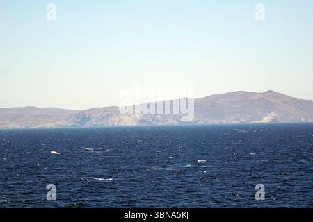 Griechische Inseln zwischen Zypern und Athen., Ein riesiges tiefblaues Meer mit kleinen Wellen, die sanft gegen die Küste plätschern. Der Horizont ist von einer Reihe brauner und brauner Berge geprägt, deren Gipfel bis zum klaren, hellblauen Himmel reichen. Die Berge scheinen von Vegetation bedeckt zu sein, obwohl die Details nicht deutlich sichtbar sind. Der Himmel ist hellblau, ohne sichtbare Wolken. Das Bild wurde aus der Ferne aufgenommen und bietet einen weiten Blick auf das Meer und die fernen Berge. Das Auge und die Phantasie eines Künstlers Stockfoto