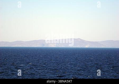 Griechische Inseln zwischen Zypern und Athen. Ein riesiges tiefblaues Meer, das sich bis zum Horizont erstreckt. Der Horizont ist von einer Reihe hellbrauner und hellbrauner Berge geprägt, deren Gipfel bis zum klaren, hellblauen Himmel reichen. Die Berge scheinen von Vegetation bedeckt zu sein, obwohl die Details nicht deutlich sichtbar sind. Der Himmel ist hellblau, ohne sichtbare Wolken. Das Bild wurde aus der Ferne aufgenommen und bietet einen weiten Blick auf das Meer und die fernen Berge. Das Auge und die Phantasie eines Künstlers Stockfoto