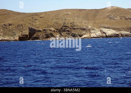 Griechische Inseln zwischen Zypern und Athen. Eine felsige Küste mit tiefblauem Meer. Das Meer ist von kleinen Wellen gespickt, und der Himmel ist klar, hellblau. Die Küste besteht hauptsächlich aus braunen und braunen Felsen, mit einigen Bereichen aus leichterem, möglicherweise weißem Gestein. Die Perspektive des Bildes ist vom Meer aus und blickt auf die Küste. Der Himmel ist klar und hell, was auf einen sonnigen Tag hindeutet. Das Auge und die Phantasie eines Künstlers Stockfoto