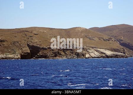 Griechische Inseln zwischen Zypern und Athen. Eine felsige Küste mit einem tiefblauen Ozean im Vordergrund. Die Küste ist durch eine Reihe von braunen und braunen Hügeln gekennzeichnet, wobei einige Gebiete karger erscheinen als andere. Die Hügel sind mit Vegetation bedeckt, darunter einige grüne Flecken, und zeigen Anzeichen von Erosion oder Verwitterung. Der Himmel ist klar, hellblau und das Wasser ist relativ ruhig mit kleinen Wellen. Die Perspektive des Bildes ist vom Ozean aus, blickt auf die Küste und erzeugt ein Gefühl von Tiefe und Distanz. Das Auge und die Phantasie eines Künstlers Stockfoto