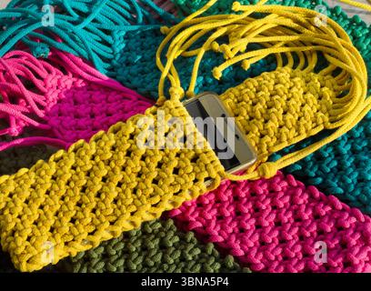 Eine lebendige Nahaufnahme handgestrickter Macramé-Smartphone-Taschen. Eine Kollektion handgefertigter Accessoires in Türkis, Fuchsia, Oliven und Gelb Stockfoto