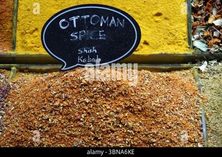 Istanbul, Türkei. Die größte Stadt in der Türkei und eine der wenigen transkontinentalen Städte der Welt, die sich über Europa und Asien auf der Bosporus-Straße erstreckt. Ein pulsierendes Gewürzangebot an einem Marktstand. Ein großer Haufen roter und orangener Gewürze, darunter wahrscheinlich auch Schaschlik, dominiert den Vordergrund. Hinter dem Stapel befindet sich ein gelber Behälter, in dem eine Mischung aus Gewürzen enthalten ist, darunter scheinbar getrocknete Kräuter oder Gewürze. Ein schwarzes Schild mit weißem Text mit der Aufschrift „Spice Shish Kebab“ ist in der Bildmitte deutlich sichtbar und zeigt die Art des verkauften Gewürzes an. Das Schild ist an einem Holz befestigt Stockfoto