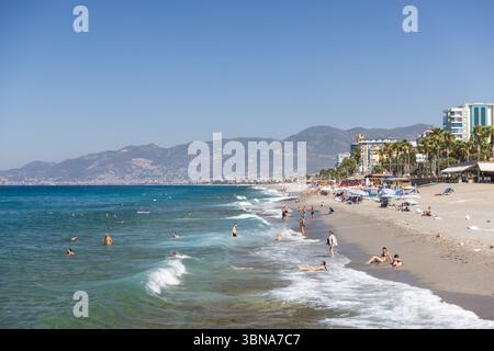 Mahmutlar, Türkei - 13. August 2024: Die Menschen entspannen und schwimmen an einer wunderschönen Küste mit klarem blauem Wasser und fernen Hügeln Stockfoto