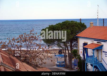 Latsi (Latchi), Zypern. Die Nordwestküste Zyperns im Bezirk Paphos, nahe der Stadt Polis. Entspanntes, malerisches Dorf am Meer, bekannt für seinen Yachthafen, frische Meeresfrüchte und ruhige Strände. Eine ruhige Küstenlandschaft mit einem weißen Gebäude mit rotem Dach und blauer Zierleiste, gelegen auf einem kleinen, gepflasterten Gebiet nahe dem Ufer. Ein blauer Pavillon mit weißem Vordach befindet sich in der Nähe des Gebäudes. Ein kleines, helles Fahrzeug parkt in der Nähe des Pavillons. Ein kleines, helles Fahrzeug parkt in der Nähe des Stockfoto