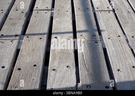Limassol, Zypern, Nahaufnahme einer hölzernen Oberfläche aus vertikalen Dielen. Die Dielen sind verwittert und zeigen Alterserscheinungen mit einem gräulich-braunen Farbton. Jede Diele ist mit einer Reihe kleiner, runder Löcher gesichert, und die Dielen sind versetzt angeordnet, um ein Gefühl von Tiefe zu erzeugen. Die Perspektive ist aus einem niedrigen Winkel und blickt auf die Dielen, was ein Gefühl von Skala vermittelt und die Textur des Holzes betont. Die Dielen sind diagonal angeordnet, wobei die linke obere Ecke des Bildes einen Teil der Dielen zeigt. Der Hintergrund ist verschwommen, wodurch der Fokus auf das Holz fällt Stockfoto