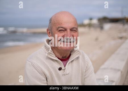 Älterer portugiesischer Mann, der am Meer sitzt und auf den Ozean blickt Stockfoto