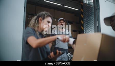 Multiethnische Mitarbeiter entladen Kartonschachteln mit Online-Bestellungen im E-Commerce. Weibliche Führungskraft mit Tablet-Computer und Barcode-Scanner. Expressversand. Außerhalb des Logistics Retail Warehouse. Stockfoto