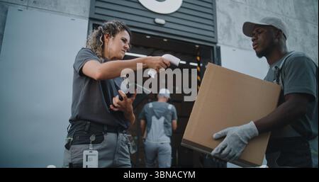 Verschiedene Mitarbeiter, die Kartons zum Logistiklager transportieren. Weibliche Koordinatorin scannt Pakete mit Barcode-Scanner mit digitalem Tablet. Online-Bestellungen, Lieferungen und E-Commerce-Waren. Stockfoto