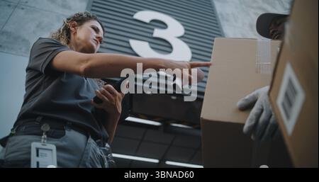 Multiethnische Arbeiter bringen Kartons mit Online-Bestellungen, E-Commerce-Waren zum Logistiklager. Weiblicher Manager scannt Pakete mit Barcode-Scanner mit Tablet-Computer. Aufnahmen Mit Niedrigem Winkel. Stockfoto