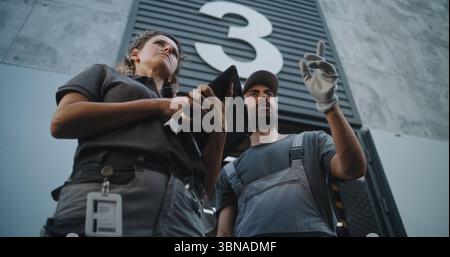 Verschiedene Mitarbeiter, die Kartons zum Logistiklager transportieren. Weibliche Koordinatorin scannt Pakete mit Barcode-Scanner mit digitalem Tablet. Online-Bestellungen und E-Commerce-Waren. Aufnahmen Mit Niedrigem Winkel. Stockfoto