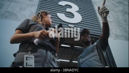 Verschiedene Mitarbeiter, die Kartons zum Logistiklager transportieren. Weibliche Koordinatorin scannt Pakete mit Barcode-Scanner mit digitalem Tablet. Online-Bestellungen und E-Commerce-Waren. Aufnahmen Mit Niedrigem Winkel. Stockfoto