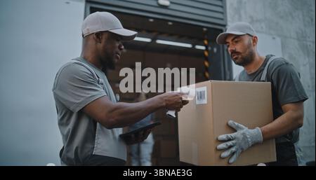 Verschiedene Mitarbeiter, die Kartons zum Logistiklager transportieren. Afroamerikaner-Koordinator scannt Pakete mit Barcode-Scanner mit digitalem Tablet. Online-Bestellungen, Lieferung, E-Commerce-Waren. Stockfoto