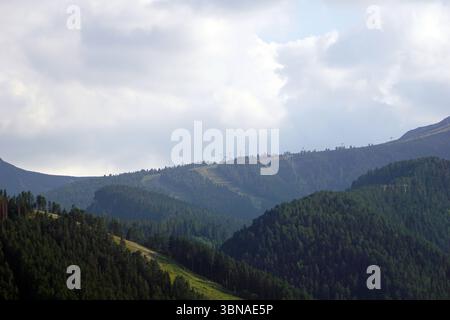 Eine bergige Landschaft mit einer Mischung aus Grün- und Brauntönen. Die Berge sind von einem dichten Wald von Bäumen bedeckt, wobei einige Bereiche hellgrün sind, was möglicherweise auf Gras oder andere Vegetation hinweist. Der Himmel ist voller Wolken, die ein weiches Licht über die Szene werfen. In der Ferne ist an den Berghängen ein Skilift oder ein ähnliches Bauwerk zu sehen. Die Berge scheinen Teil einer Gebirgskette zu sein, mit einer Reihe von Gipfeln und Tälern, die im Bild zu sehen sind. Bansko ist eine malerische Stadt im Südwesten Bulgariens am Fuße der Stockfoto