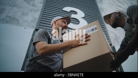 Außerhalb des Logistics Retail Warehouse: Mitarbeiter nimmt Karton mit Online-Bestellungen und E-Commerce-Waren vom afroamerikanischen Mitarbeiter des Express Delivery Service. Aufnahmen Mit Niedrigem Winkel. Zeitlupe. Stockfoto