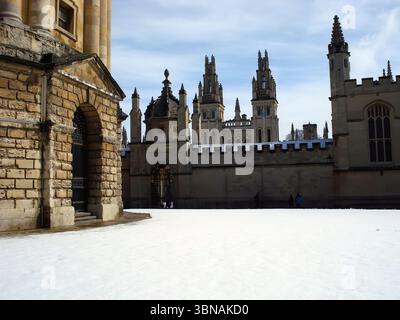 Radcliffe Camera, Bodleian Library, Oxford – die berühmte Stadt in England, die weltweit für ihre renommierte Universität und reiche Geschichte bekannt ist, Großbritannien. Ein schneebedeckter Innenhof vor einem großen, reich verzierten Steingebäude mit einer dunkelbraunen oder schwarzen Tür. Der Innenhof ist von einer Steinmauer mit einer zinnenförmigen Spitze umgeben, und das Gebäude verfügt über mehrere Türme und Türme. Der Himmel ist ein klares Blau mit ein paar Wolken. Der Boden ist mit einer Schneeschicht bedeckt, und einige Menschen können in der Entfernung gesehen werden. Das Auge und die Phantasie eines Künstlers Stockfoto