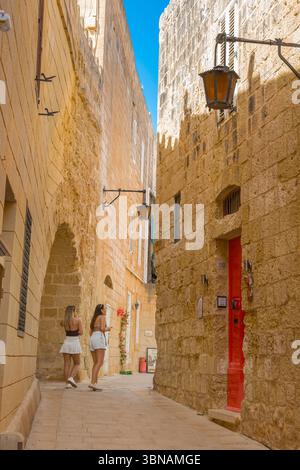 Mdina Malta Street, Blick im Sommer auf zwei junge weibliche Touristen, die eine enge, gewundene Straße in der historischen ummauerten Stadt Mdina, Malta, erkunden Stockfoto