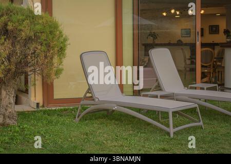 Sonnenliegen auf dem Rasen vor dem Restaurant. Zwei graue Liegestühle in der Nähe des Hauses Stockfoto