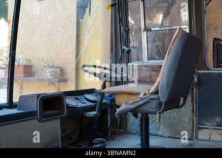 Nikosia (Lefkosia), Zypern, die letzte geteilte Hauptstadt der Welt, das Bild zeigt das Innere eines alten Busses, der wahrscheinlich verlassen wurde oder sich in einem Zustand befindet. Der Innenraum des Busses wird von einem schwarzen Lenkrad und einem grauen Sitz dominiert, der aus abgenutztem Stoff besteht. Der Sitz ist leicht nach links geneigt. Das Armaturenbrett ist mit einem schwarzen Lenkrad und einem Bedienfeld mit verschiedenen Tasten und Drehrädern sichtbar. Der Innenraum des Busses besteht hauptsächlich aus Holz und Metall und verfügt über ein Fenster, das mit einem Bordstein versehen ist. Der Fensterrahmen besteht aus Holz und Metall und die Fensterscheibe ist gebrochen. Der Bus Stockfoto