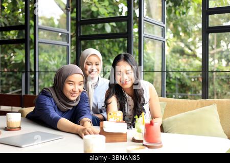 Eine Gruppe fröhlicher und hübscher asiatischer Freundinnen genießt Essen, Trinken und hängt in einem Restaurant oder Café mit Green Plant Outdoor ab Stockfoto
