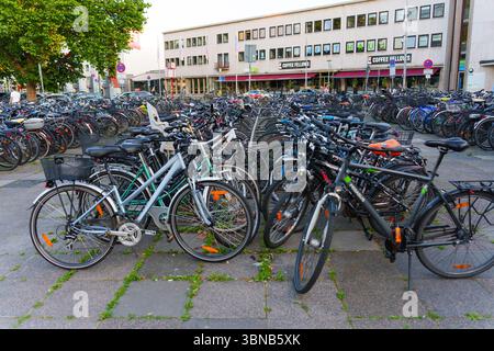 Heidelberg, Deutschland - 21. Juni 2025: Belebter städtischer Fahrradparkplatz mit verschiedenen Fahrrädern in der Nähe eines Coffeeshops bei Morgenlicht. Stockfoto