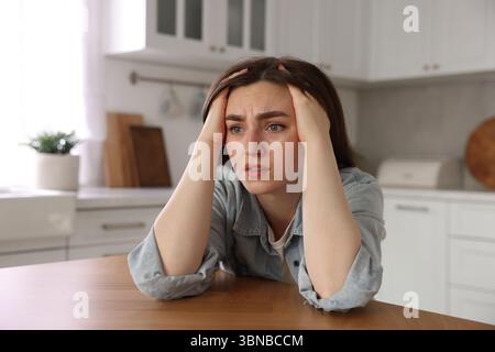 Verängstigte Frau, die an Paranoia leidet, am Tisch in der Küche Stockfoto