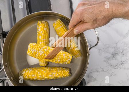 Entfernen Sie von Hand Mais auf dem Kolben aus dem Topf mit kochendem Wasser in der Küche, USA Stockfoto