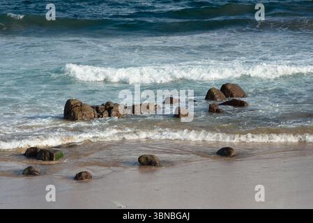 Dunkle Felsen an der Küste eines wunderschönen Strandes. Wellen brechen auf dem Sand, Paradies. Brasilien Stockfoto