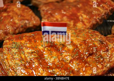 Close up BBQ Schweinerippchen glasiert mit Sauce, Oregano Streusel, gegrillt auf Holzkohle mit niederländischer Flagge, rauchiges, leckeres Street Food. Stockfoto